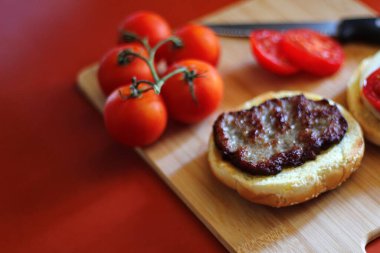 Hamburger dilimlenmiş domates, soğan ve turşuyla servis ediliyor. Mutfaktaki tahta kesme tahtasının üzerinde.