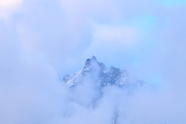 This landscape photo was taken in Europe, in France, in the Alps, towards Chamonix, in summer. We see the Aiguille du Midi in the fog in the Mont Blanc massif, under the Sun.