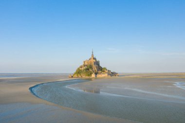 Bu manzara fotoğrafı ilkbaharda Avrupa, Fransa, Normandiya, Manche 'de çekildi. Le Mont-Saint-Michel 'i nehre ve Manş Denizi' ne bakan güneşin altında görüyoruz..