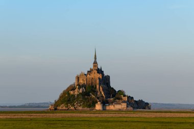 Bu manzara fotoğrafı ilkbaharda Avrupa, Fransa, Normandiya, Manche 'de çekildi. Kırsalın ortasında, güneşin altında Le Mont-Saint-Michel 'i görüyoruz..