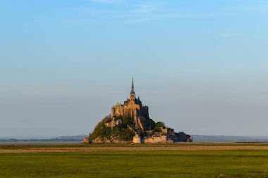 Bu manzara fotoğrafı ilkbaharda Avrupa, Fransa, Normandiya, Manche 'de çekildi. Güneşin altında Le Mont-Saint-Michel 'i ve çayırları alçak sularda görebiliriz..