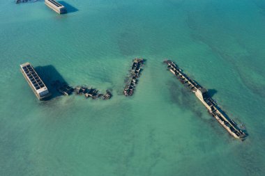 Bu manzara fotoğrafı yazın Avrupa, Fransa, Normandiya, Arromanches les Bains 'de çekildi. Asnelles 'deki yapay Altın Limanı' nın birkaç sualtı elementi güneş altında, yukarıdan görüldü..
