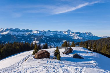 Bu manzara fotoğrafı Avrupa 'da, Fransa' da, Rhone Alpes 'te, Savoie' de, Alpler 'de, kışın çekildi. Chaine des Aravis 'e bakan bir dağın tepesinde, güneşin altında Chalets' i görüyoruz..