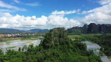 Yazın, güneşli bir günde, Vientiane ve Luang Prabang arasında, Asya 'daki Vang Vieng kasabasının önündeki çeltik tarlalarına bir karst zirvesi hakim olur..