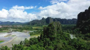 Yazın, güneşli bir günde, Vientiane ve Luang Prabang arasında, Asya 'daki Vang Vieng şehrinin önündeki suların üzerinde pirinç tarlaları olan bir karst zirvesi..