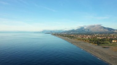 Avrupa, İtalya ve Calabria 'daki Tyrhenian Denizi' ndeki Fiumicello 'ya doğru dağların eteklerindeki uzun volkanik kum plajı güneşli bir günde.