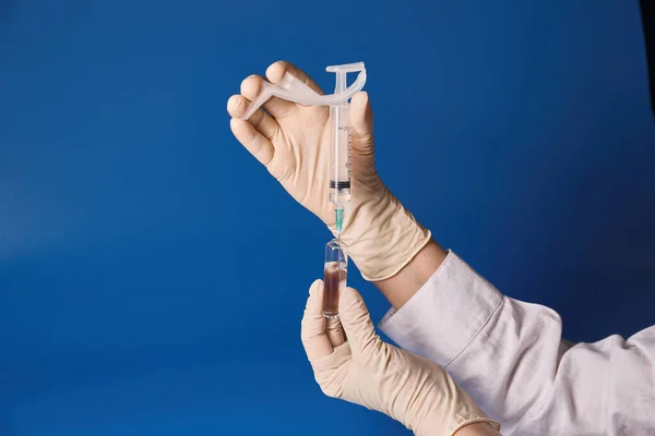 Gloved hand holding syringe on blue background — Stock Photo, Image