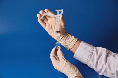 Eldivenli elini şırınga mavi arka plan üzerinde tutan 