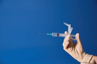 Eldivenli elini şırınga mavi arka plan üzerinde tutan 