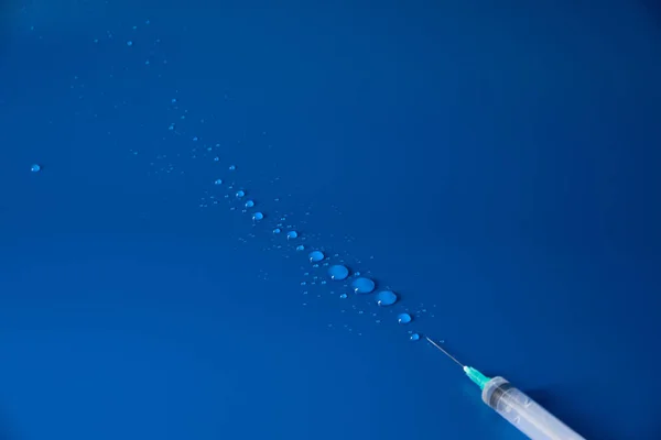 Syringe and drops of medicine lie on blue background — Stock Photo, Image