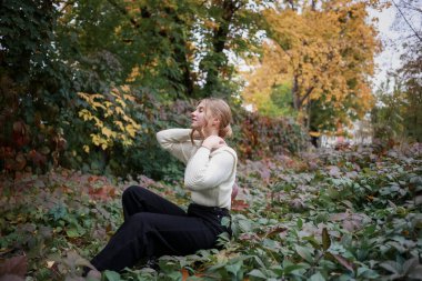 Güzel saç stili olan tatlı bir kız, kapalı gözlerle bahçede oturuyor.