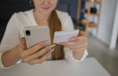 Elinde cep telefonu ve elinde kredi kartı olan genç bir kız.