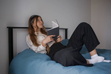 Kafasında bandaj, yatağında uzun sarı saçları olan genç bir kız elinde bir kitap tutuyor ve yan tarafa bakıyor.