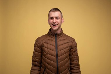 Stüdyo portresi. Sarı arka planda, kahverengi ceketli genç bir adam, şaşırmış görünüyor.