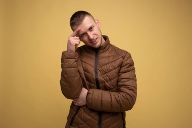 Stüdyo portresi. Sarı arka planda, kahverengi ceketli genç bir adam, şaşırmış görünüyor.