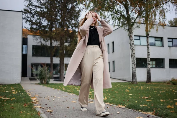 Paltolu güzel bir kız, güvenle caddede yürür, saçını düzeltir.