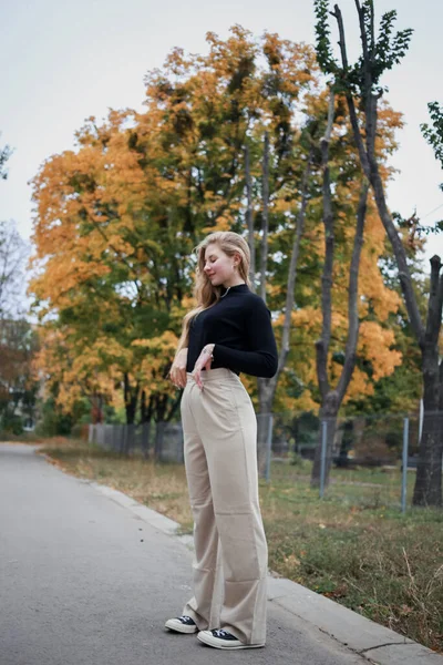 Siyah kazaklı ve pantolonlu bir kız büyük bir portakal ağacının arkasında duruyor.