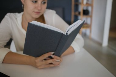 Beyaz gömlekli bir iş kadınının genç ve başarılı çalışanı elinde mavi bir not defteri ile modern bir ofisteki dizüstü bilgisayarla beyaz bir masa başında oturuyor. Kariyer başarısı, başarı ve kişisel büyüme kavramı