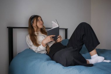 Kafasında bandaj, yatağında uzun sarı saçları olan genç bir kız elinde bir kitap tutuyor ve yan tarafa bakıyor.