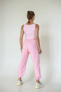 Şık giyimli bir kız, parlak bir arka plan karşısında rahat bir spor giyim, bir dergi için stüdyo çekimi, kumaş ve çiçeklerle ilgili detaylar.