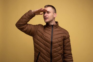 Stüdyo portresi. 20 'li yaşlarda, kahverengi ceketli, sarı arka planda genç bir adam elini yüzüne koyar ve uzaklığa bakar.