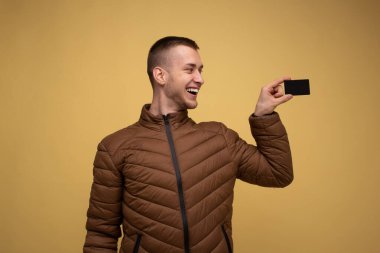 Sarı arka planda kahverengi ceketli genç bir adam elinde kredi kartı tutuyordu. Zenginlik Kariyeri Başarı Konsepti