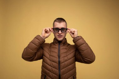 20 'li yaşlarda, sarı arka planda kahverengi ceketli genç bir adam gözlüğünü 3D film izleyecek şekilde ayarlıyor.