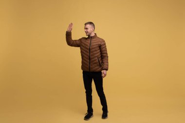 Sarı arka planda, kahverengi ceketli, 20 yaşında olağandışı bir genç adam buluşmayı hoş karşılar ve birinin izole olduğunu fark ettiğinde elini sallar.