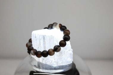 Farklı renklerde doğal taşlardan yapılmış bir bilezik büyük şeffaf bir taşın üzerinde yatar.