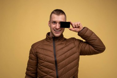 Sarı arka planda kahverengi ceketli genç bir adam elinde bir kredi kartı kılıfı tutuyor ve gözlerini kapatıyor.