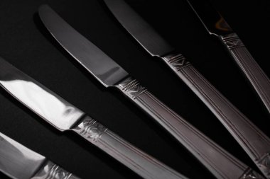 Knives made of metal, silver, lie on a black background with a glare of light