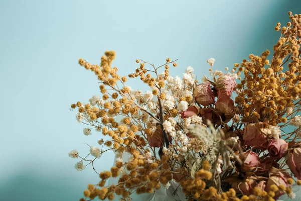 Kurumuş sarı ve pembe renkli çiçekler mavi bir arkaplanda dururlar.
