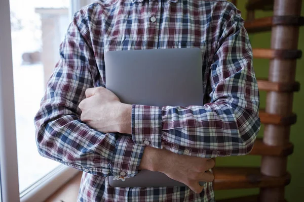 Ekose gömlekli bir adam dizüstü bilgisayarı sıkıca tutuyor.