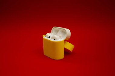 Kırmızı arka planda sarı kablosuz kulaklık.