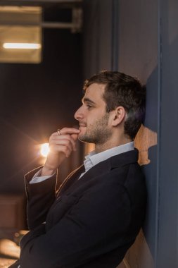 Gömlek ve ceket giymiş Gürcü bir adam duvarın yanında duruyor.