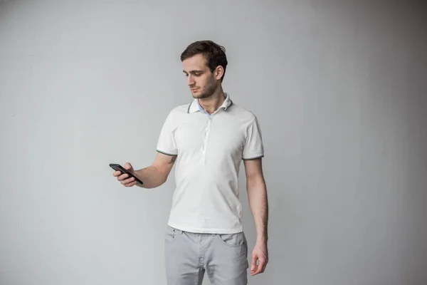 Elinde telefon tutan beyaz tişörtlü bir adam.