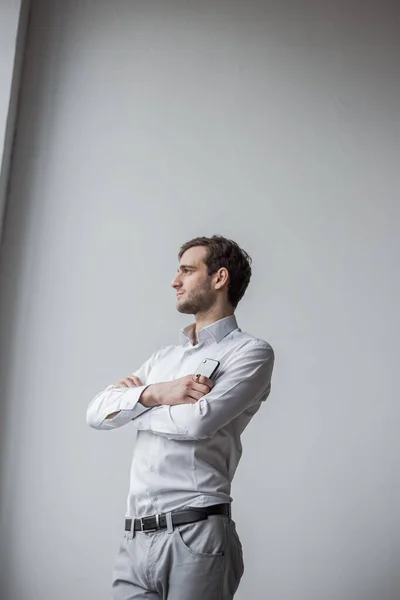 Beyaz gömlekli bir adam kollarını kavuşturmuş duruyor.