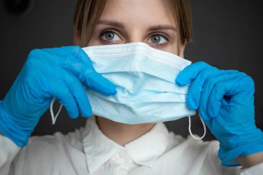 A nurse in blue gloves puts a mask on her face