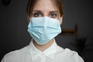 A nurse wearing blue gloves and a protective mask looks into the camera