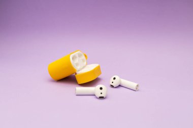 Mor arka planda sarı bir çantadaki kablosuz kulaklıklar.