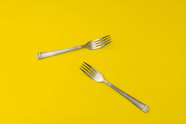 Gümüş çatallar sarı arka planda yatar, minimalizm.