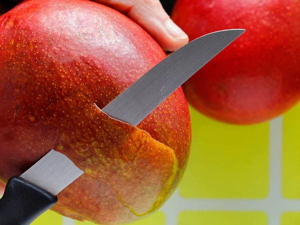 Mango soyuyordum. Meyveyi tutan bir elin ve kabuğu kesen bir bıçağın yakın plan fotoğrafını çek. Yemek için meyve hazırlıyorum.