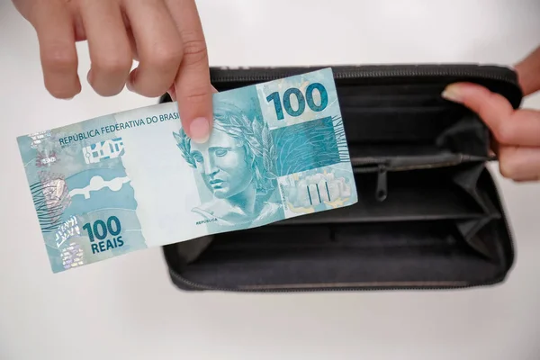 Siyah cüzdan ve mavi el ile 100 reais banknot.