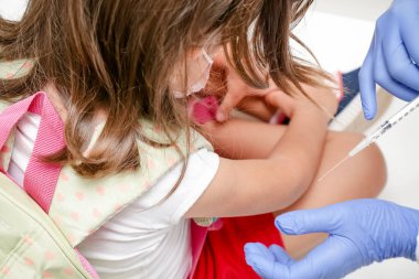 Child being vaccinated against covid 19 goes back to medical school with blue glove and syringe.