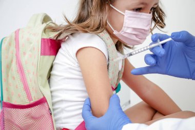 Child being vaccinated against covid 19 goes back to medical school with blue glove and syringe.