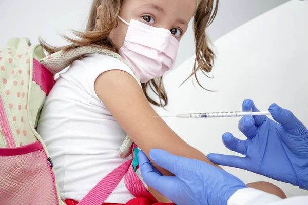 Child being vaccinated against covid 19 goes back to medical school with blue glove and syringe.