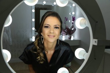 Güzel bir kadın aynanın önünde beyaz arka plan ışığı için makyaj yapıyor..