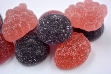 Meyve, frenk üzümü, üzüm, ahududu, yabanmersini, çilek şeklinde parlak kiraz, kırmızı, mor, pembe, lezzetli şekerler. Çeşitli jöleli şekerler, tüm renkler beyaz arka planda bulunur..