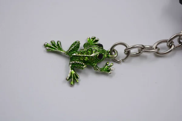 一个漂亮的 明亮的钥匙链装饰着绿色的小青蛙 蛤蟆与绿色的小石头 三只装饰钥匙的小青蛙的金属链上的珠宝 — 图库照片