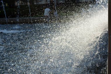 Bright splashes of clean water, jets, drops scatter from the fountain against the backdrop of the sun's rays.
